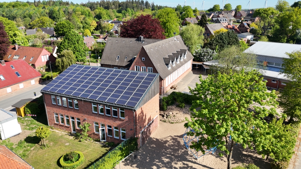 Luftaufnahme unserer Grundschule in Holtsee mit Blick auf den Schulhof und Spielplatz.